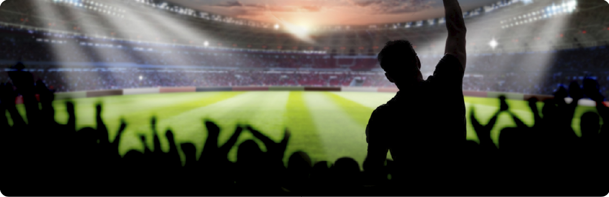 Siluetas de personas aficionadas celebran desde las gradas de un estadio de fútbol iluminado.