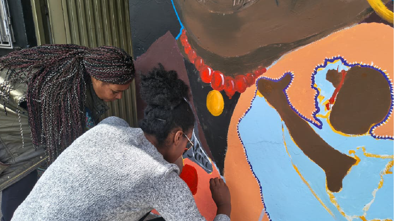 Lideresas de Barrios Unidos pintan los detalles de un mural que representa memoria e identidad afro, en un proceso comunitario acompañado por IDPAC en Bogotá.