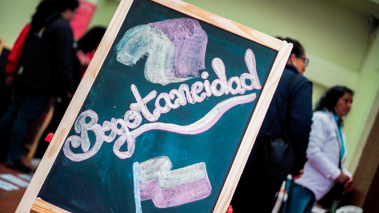 Tablero con la palabra “Bogotaneidad” escrita con tiza y decorado con banderas, en un evento del IDPAC con participación ciudadana.