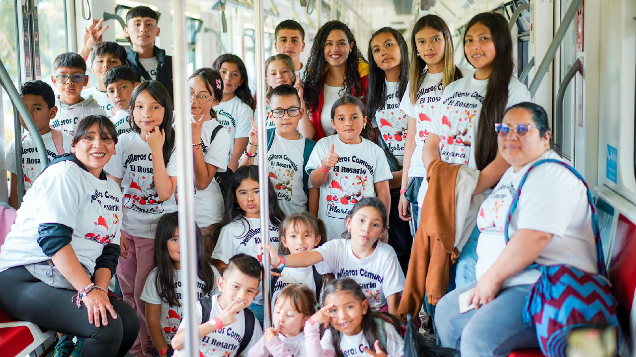 Niñas y niños de los Semilleros Comunales El Rosario posan juntos dentro de un vagón del Metro de Bogotá durante el Festival INN Comunalitos, acompañados por sus cuidadoras y lideresas comunitarias.