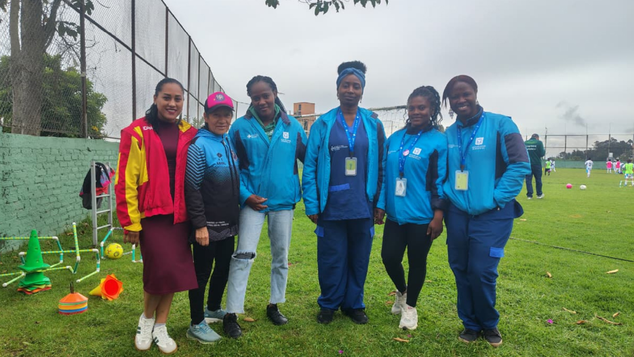 Equipo del IDPAC y lideresas comunitarias posan en una cancha de fútbol en Usaquén durante una jornada de salud y socialización de la estrategia étnica para deportistas.