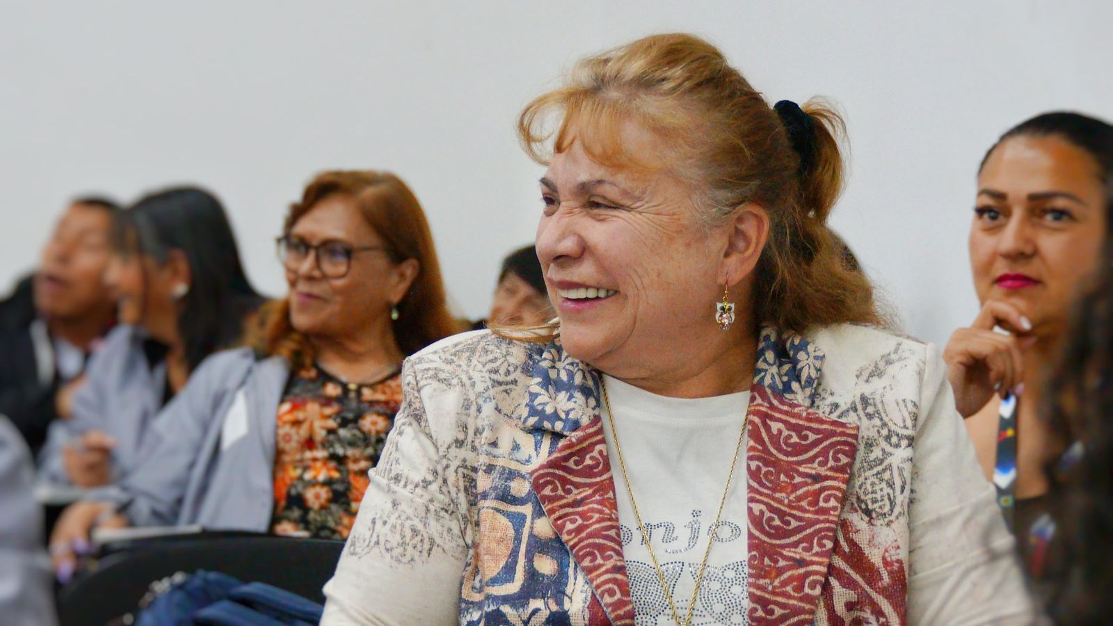 Mujer mayor sonríe durante un encuentro institucional con otras personas participantes, en un espacio de diálogo y fortalecimiento de la participación ciudadana en Bogotá.