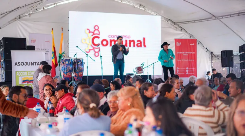 Líderes y comunidad participan en un Congreso Comunal Local en Bogotá, con escenario principal, panelistas y mesas de trabajo bajo una carpa.