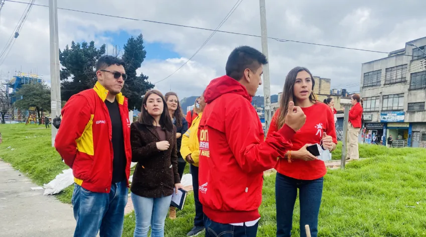 Grupo de funcionarios del IDPAC y la Alcaldía Local dialogando durante una visita territorial en el barrio La Fragüita, en un espacio verde donde realizan diagnóstico y trabajo comunitario.