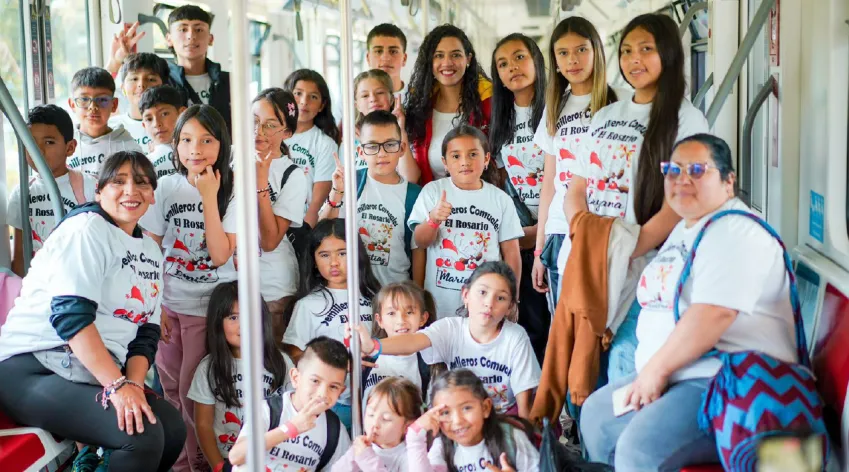 Niñas y niños de los Semilleros Comunales El Rosario posan juntos dentro de un vagón del Metro de Bogotá durante el Festival INN Comunalitos, acompañados por sus cuidadoras y lideresas comunitarias.