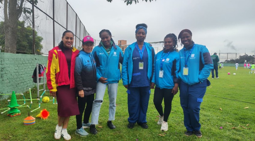 Equipo del IDPAC y lideresas comunitarias posan en una cancha de fútbol en Usaquén durante una jornada de salud y socialización de la estrategia étnica para deportistas.